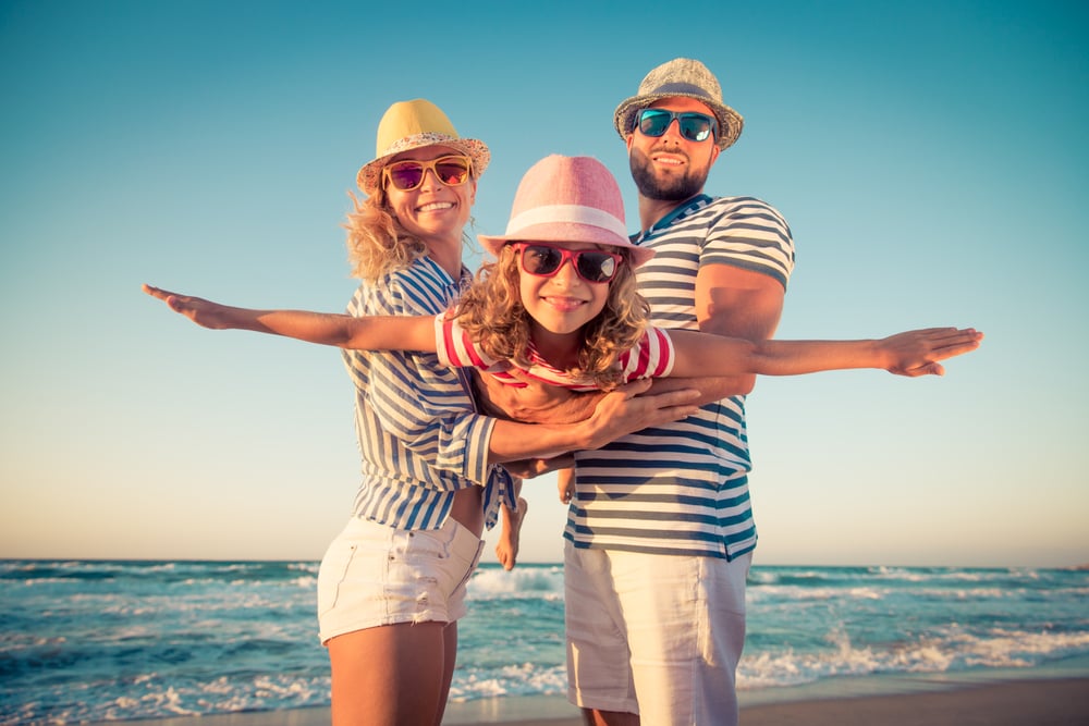 Una familia disfruta de sus vacaciones en la playa. Los padres elevan a su hija como si volara en avión